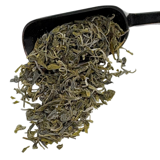 Black scoop filled with green tea leaves on a white background
