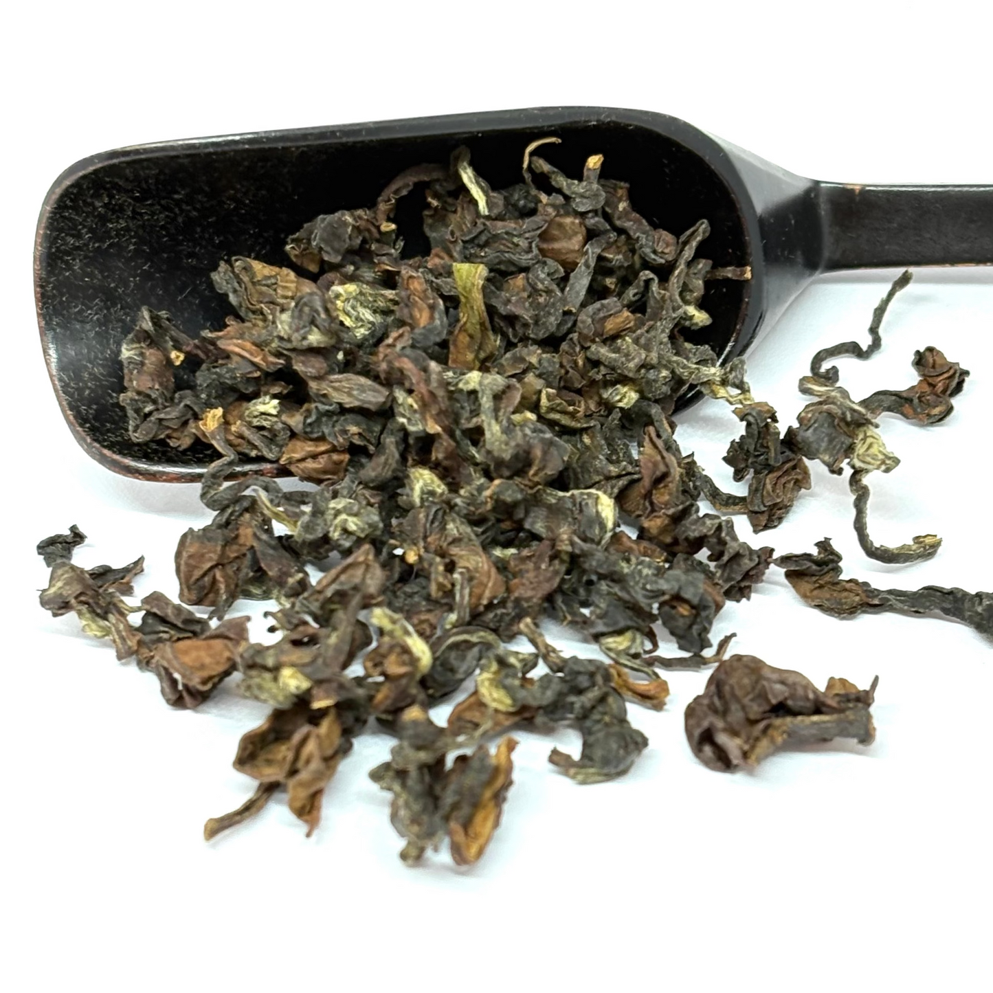 Black scoop filled with dried green tea leaves on a white background